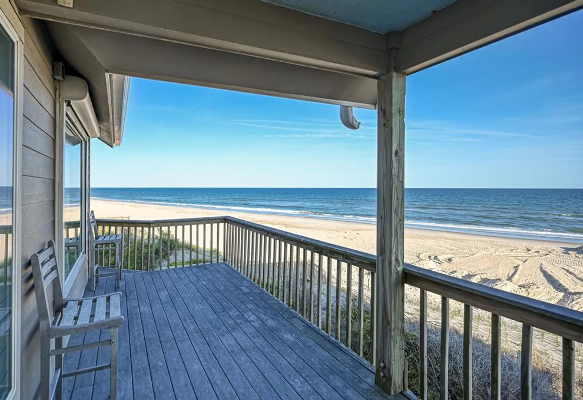 A serene view from the wooden beachfront deck, overlooking the ocean waves. The image captures the proximity of the home to the sand, showcasing direct beach access and the tranquil atmosphere of private beachfront living.