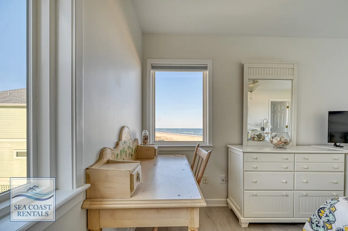 A serene interior scene with a wooden desk placed by a window overlooking the ocean, complemented by a white dresser. The workspace invites productivity, while the expansive view provides daily inspiration and moments of calm during work hours.