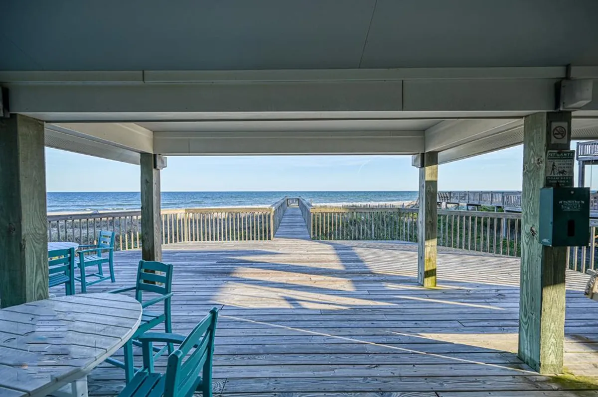An exterior shot of a wooden deck furnished with vibrant blue chairs, overlooking the endless ocean. This outdoor space invites guests to relax, enjoy meals al fresco, or simply soak in the sea breeze and horizon.
