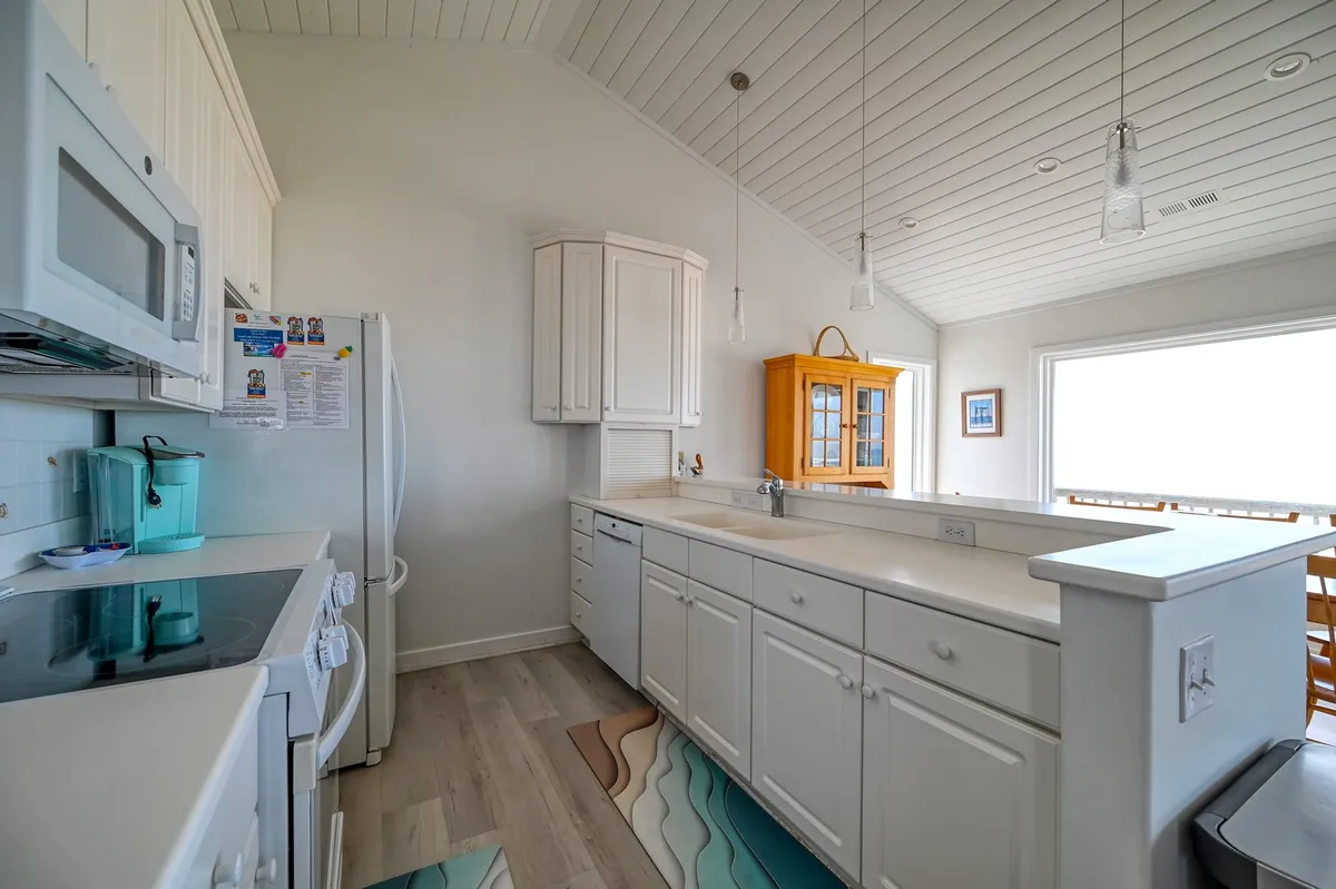 A gourmet kitchen with white cabinetry, a kitchen island, and a cheerful yellow cabinet, all illuminated by natural light. The space feels airy and modern, inviting family and friends to gather for cooking and conversation.