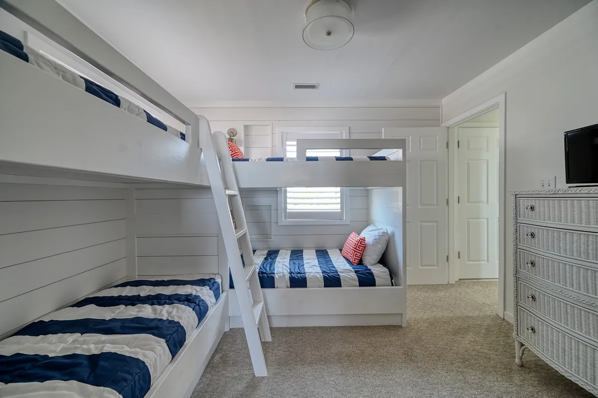 A playful and cozy bunk room with striped bedding, decorative pillows, and a dresser. The room exudes a sense of fun and comfort, ideal for children to play, socialize, and create lasting memories together.