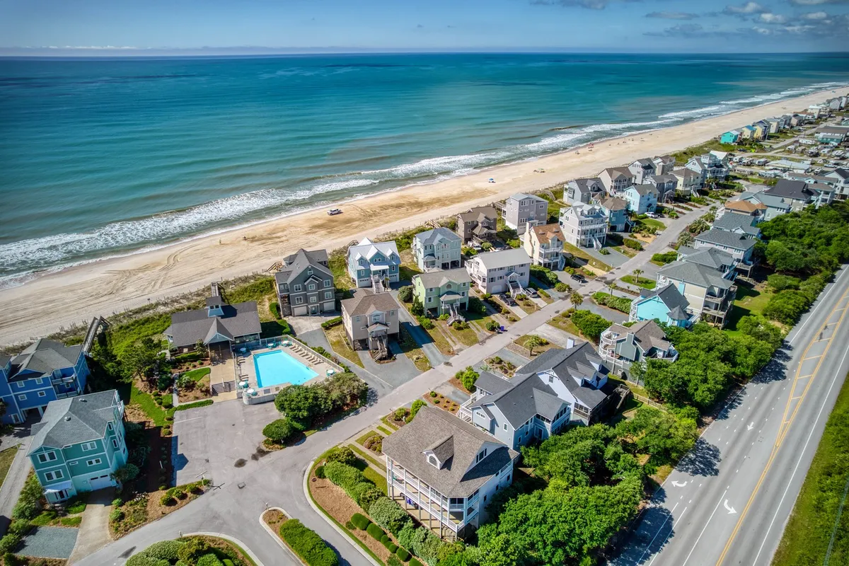 A wide exterior shot featuring the community pool with views of the ocean and adjacent homes. The pool area is inviting, surrounded by lounge chairs and greenery, perfectly set for family fun and relaxation.