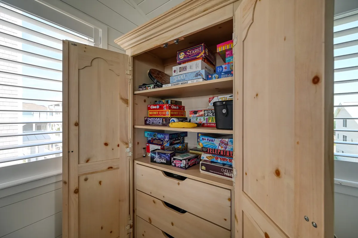 A shelving unit filled with a variety of board games and games supplies next to a wooden cabinet, inviting guests to grab a game and gather for an evening of laughter and bonding.