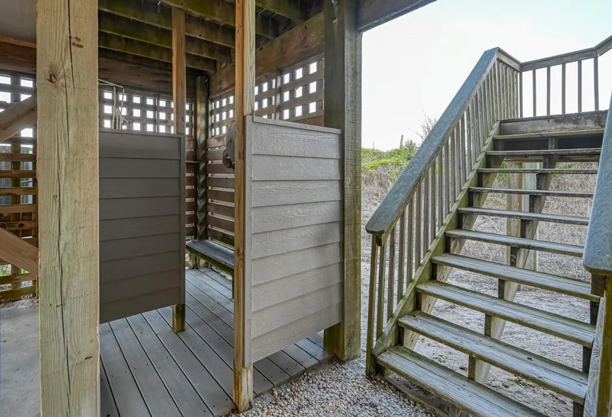 An outdoor shower area with wooden stalls and a staircase, designed for rinsing off after a day at the beach. The relaxed, casual setup emphasizes convenience and comfort for beachgoers.