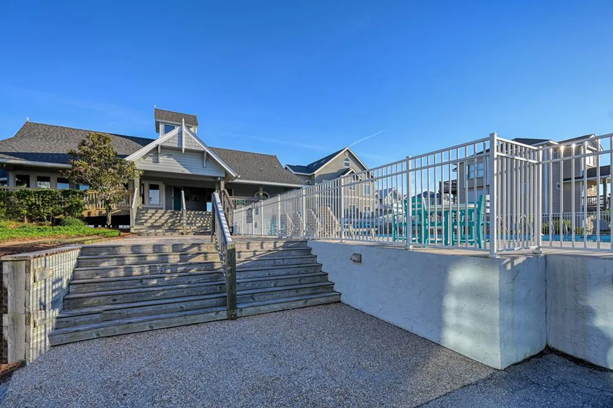 An inviting exterior shot of wooden stairs descending to a pool area surrounded by lush greenery. The space is ideal for swimming, sunbathing, and hosting social gatherings, capturing the laid-back, communal spirit of a coastal getaway.