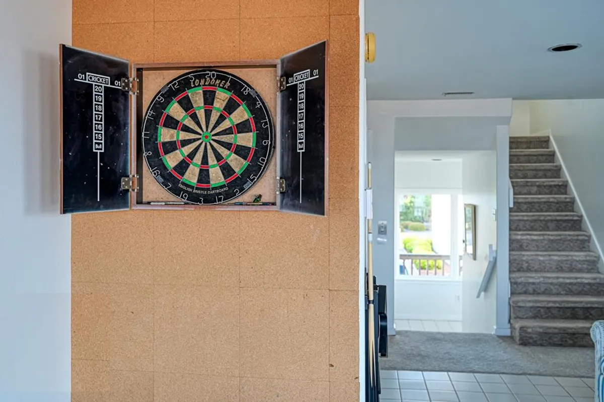 A cozy interior corner with a dartboard mounted on the wall beside a staircase, creating a natural zone for friendly dart matches and spontaneous games.