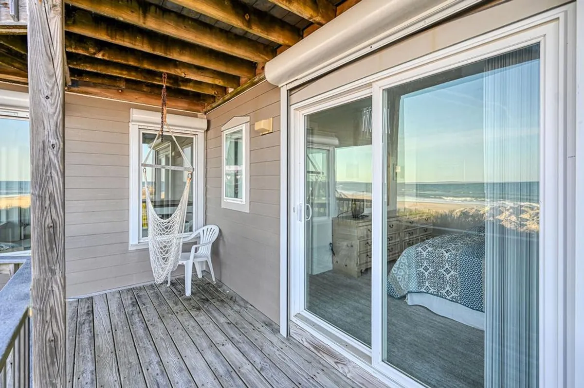 This serene exterior scene features a hammock and a white chair situated near a large glass door leading to a bedroom. The view hints at relaxation and offers a glimpse of the ocean, inviting guests to unwind after a day of local exploration.