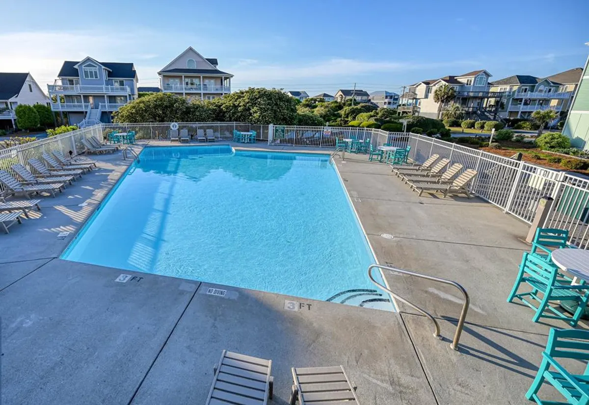 This image captures a vibrant community swimming pool surrounded by lounge chairs, outdoor tables, and lush greenery. The pool area is well-maintained and inviting, with ample space for swimming, sunbathing, and socializing. The atmosphere is relaxed yet social, reflecting the kind of activity and community engagement described in the section.