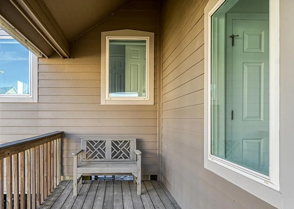 This exterior image features a wooden bench situated next to the home's windows, with textured exterior walls in view. The scene is tranquil, suggesting a peaceful spot for breaks or contemplation while listening to the soothing sounds of nature and the ocean nearby.